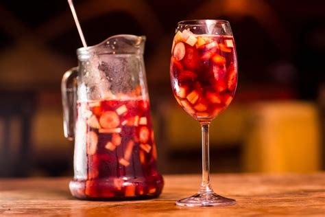 Fotografía de una jarra de sangría con frutas y hielo, servida en copas en un ambiente veraniego