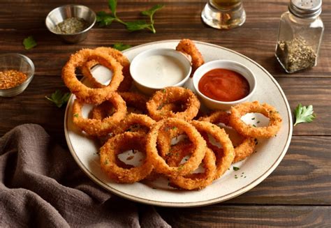 Aros de cebolla al horno dorados y crujientes con un tazón de salsa.