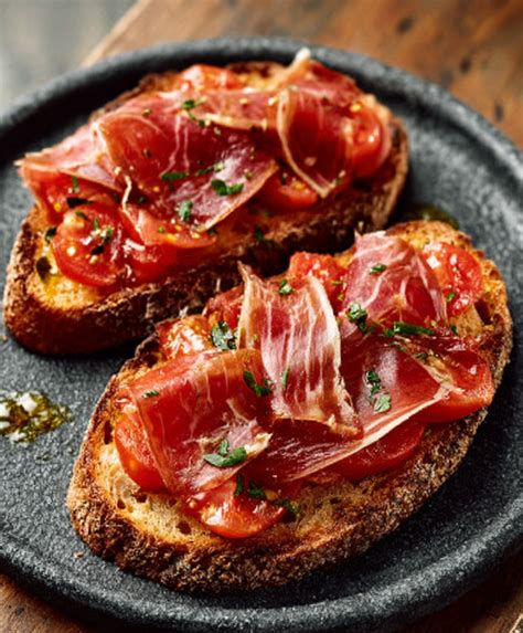 Foto de pan con tomate servido con diferentes acompañamientos como jamón y queso.
