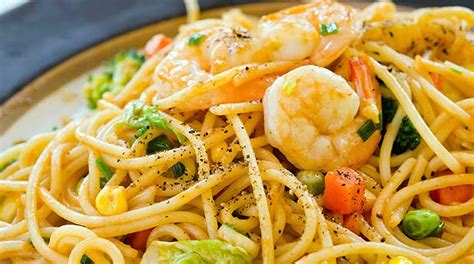 Plato de fideos con camarones picantes adornado con hierbas frescas y maní