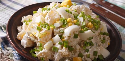 Ensalada de papa terminada, decorada con huevo duro en cuartos y hierbas frescas, servida sobre hojas de lechuga.