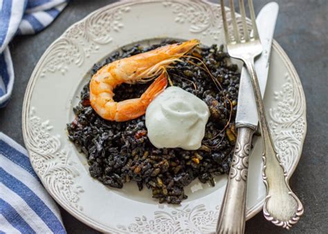 Plato de arroz negro servido con una guarnición de alioli en un entorno mediterráneo.