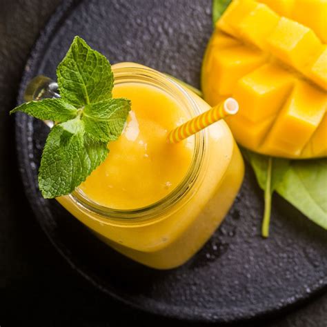 foto de un batido de mango cremoso servido en un vaso, con trozos de mango y hoja de menta de decoración