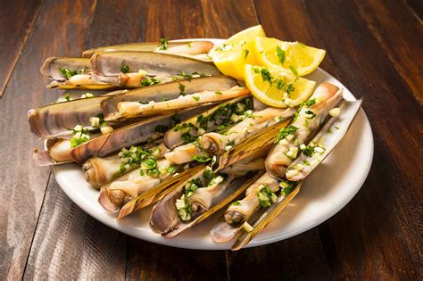 Plancha con navajas cocinándose, mostrando las conchas abiertas y el jugo soltado.