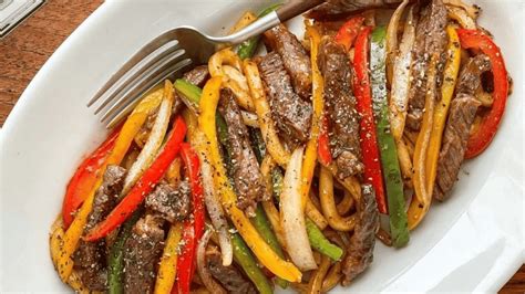 Plato de fajitas servido con tiras de carne, pimientos, cebolla y tortillas de trigo calientes.