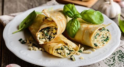 Imagen de los panqueques rellenos dispuestos en capas, cubiertos con salsa blanca.