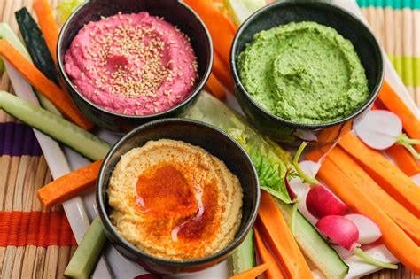 Tabla con tres cuencos de hummus de diferentes colores: clásico, remolacha y pimiento rojo