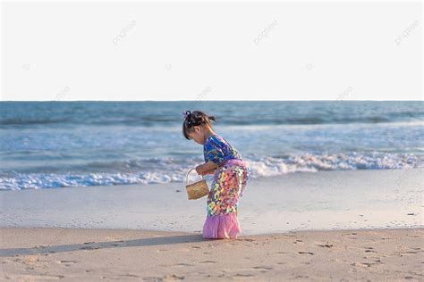 Una niña feliz recogiendo conchas en la playa, arrodillada cerca del agua con un cubo lleno