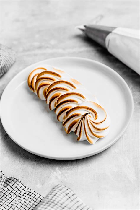 Manga pastelera creando espirales de merengue suizo sobre una base.