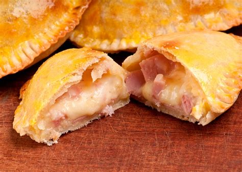 Ilustración de empanadas de jamón y queso recién hechas, con queso derretido asomando por los bordes.