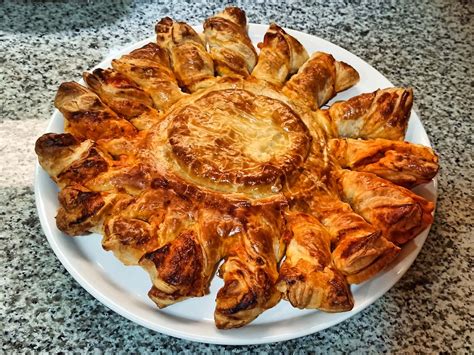 Imagen de un pastel de camembert dorado y crujiente, decorado con hojaldre en forma de hojas y semillas.