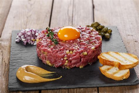 Fotografía de un steak tartar servido con estilo gourmet sobre un plato de pizarra, acompañado de yema de huevo y alcaparras.