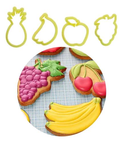 Varias galletas con forma de frutas (manzana, naranja, piña) en diferentes etapas de decoración con glaseado de colores, mostrando la técnica