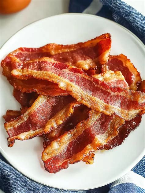 Plato con lonchas de tocino crujiente dorado sobre papel absorbente