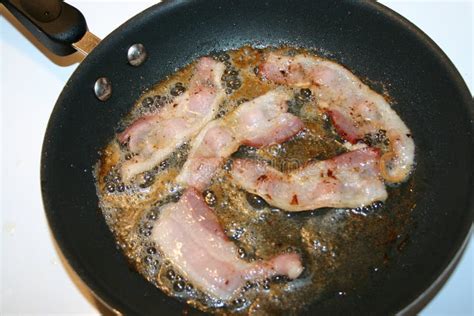 Sartén en la estufa con lonchas de tocino friéndose y una pantalla antisalpicaduras