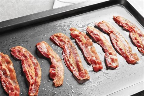 Bandeja para hornear con rejilla metálica y lonchas de tocino cocinándose en el horno