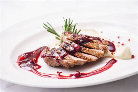 Plato de carne de ave con una generosa porción de salsa de frutos rojos brillante sobre una mesa elegante.