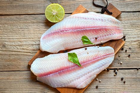 Filete de panga fresco sobre tabla de cortar con hierbas