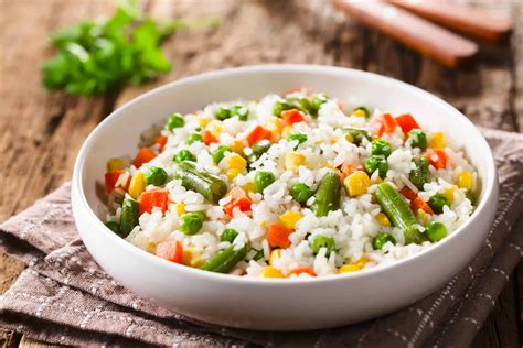 Plato de arroz a la jardinera con vegetales coloridos como zanahorias, guisantes y maíz sobre una mesa rústica.