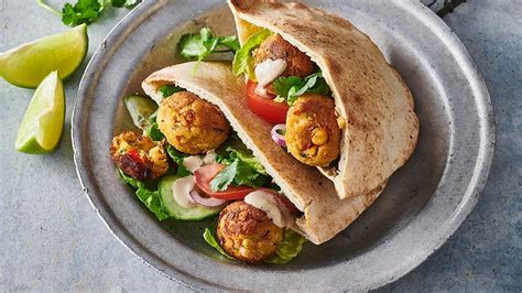Tabla de madera con varios panes de pita rellenos: uno con falafel, otro con hummus y vegetales, y uno abierto con queso y tomate.