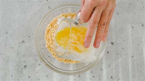 Foto de primer plano de galletas trituradas mezclándose con mantequilla derretida en un tazón de vidrio