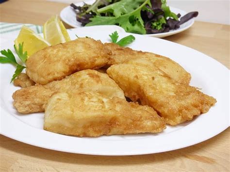 Plato de filete de merluza a la romana con rodajas de limón y una guarnición de judías verdes