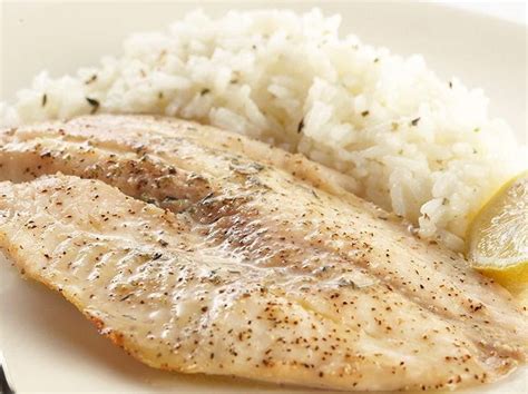 Plato de filete de pescado blanco a la plancha acompañado de una guarnición de arroz basmati con hierbas frescas y rodajas de limón