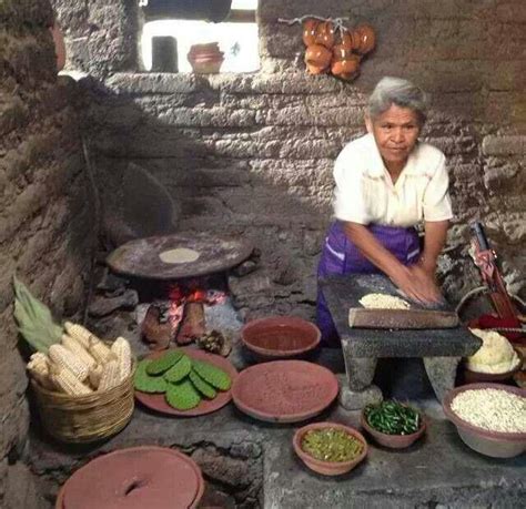 Foto histórica de mujer mixteca haciendo tortillas de maíz con metate y comal de barro sobre fogón de leña