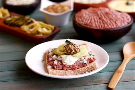 Fotografía gastronómica de un crudo chileno montado sobre una tostada, decorado con cebolla y mostaza