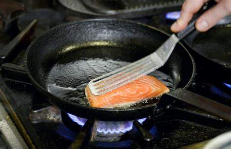 Chef sellando lomo de salmón en sartén caliente