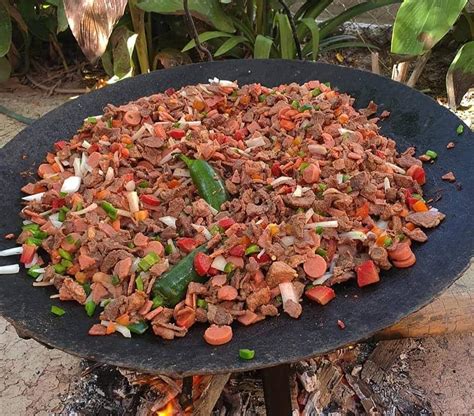 Fotografía detallada de una discada norteña servida en un disco de arado tradicional, mostrando la variedad de carnes y vegetales mezclados.