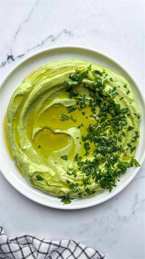 Plato de hummus verde decorado con trozos de aguacate y cilantro.