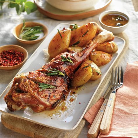 Plato de costillas de cordero al horno decorado con romero fresco y guarnición de patatas asadas