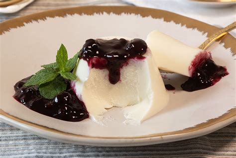 Panna Cotta clásica decorada con frutos rojos y una copa de vino blanco