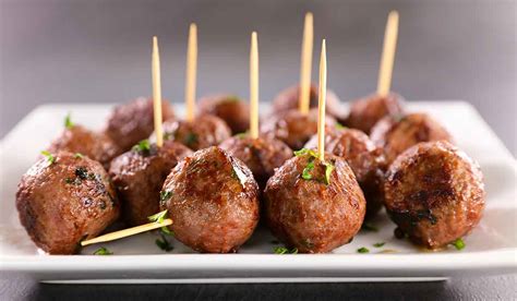 Imagen de bolitas de carne preparadas para cóctel, presentadas de forma atractiva con palillos y una salsa al lado.