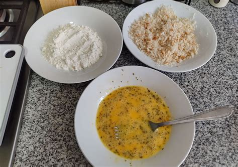 Fotografía cenital mostrando tres recipientes con harina, huevo batido y pan rallado en serie