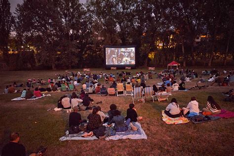 Espectadores disfrutando del cine al aire libre con palomitas en un campus universitario, con una pantalla grande y un ambiente nocturno
