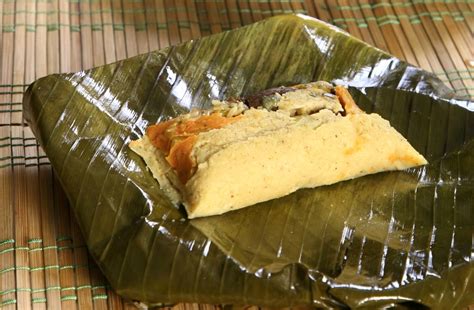 Fotografía de un tamal tradicional envuelto en hoja de plátano, listo para ser rebanado.