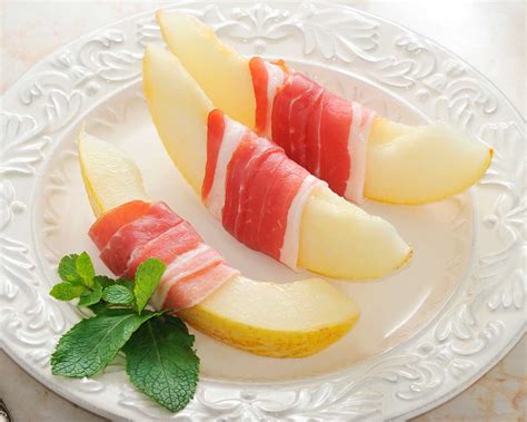 Rodajas de melón envueltas en jamón, rociadas con vinagreta y decoradas con hierbabuena.