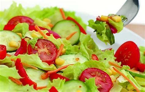 Un tarro de cristal lleno de capas coloridas de ensalada: lechuga, tomate, pepino, pimiento, zanahoria y atún, coronado con semillas.