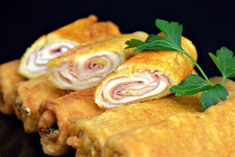 Rollitos de pan de molde rellenos con palta, jamón y queso, enrollados en papel film