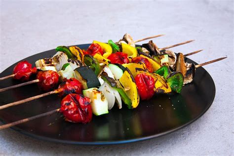 Varias brochetas veganas con coloridas verduras (pimientos, cebolla, calabacín, champiñones) asándose en una parrilla