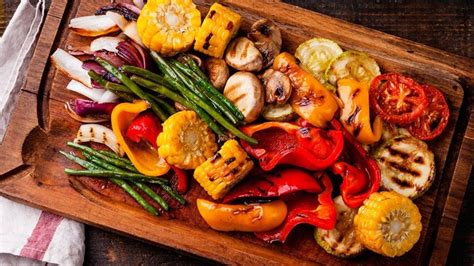Plato de asado vegano con hamburguesas vegetales, salchichas veganas y tofu a la parrilla, acompañado de verduras