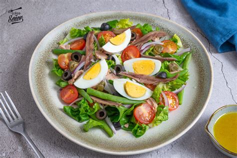 Fotografía de una ensalada Niçoise presentada de forma atractiva, mostrando sus ingredientes coloridos dispuestos armoniosamente.