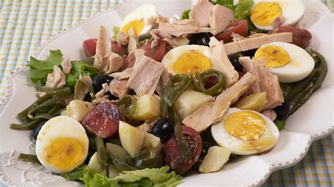 Comparativa visual:lado a lado, una representación de la ensalada Niçoise tradicional (con anchoas) y una versión moderna (con atún y papas).