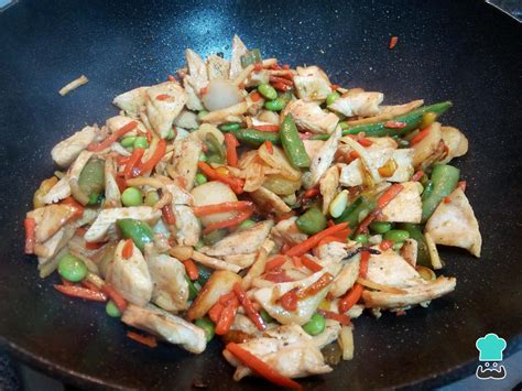 Fotografía de un wok con pollo y verduras salteándose.
