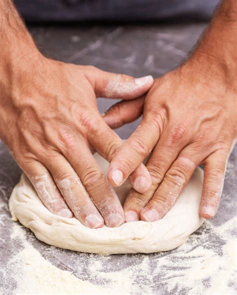 Manos estirando masa de pizza sobre una superficie enharinada.