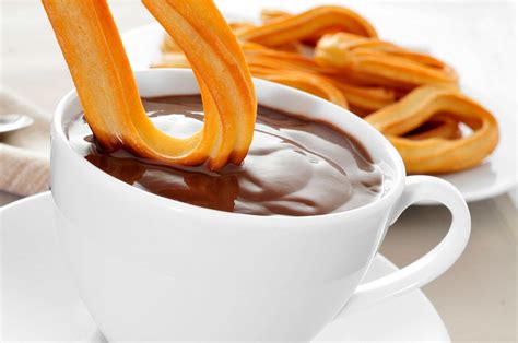 Taza de chocolate caliente con churros y chimenea de fondo