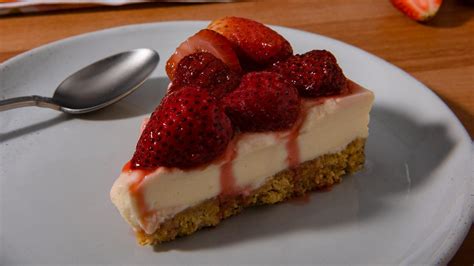 Fotografía profesional de un cheesecake de frutilla decorado con frutas frescas sobre un plato elegante.