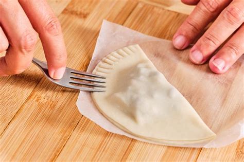 Manos formando una empanada, sellando los bordes con un tenedor y mostrando el relleno de Cordon Bleu